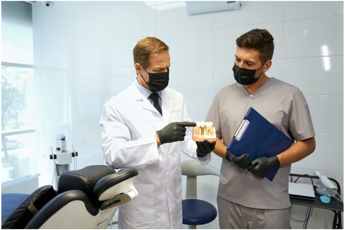 dentist pointing to a tooth model while mentoring a colleague in a dental office.